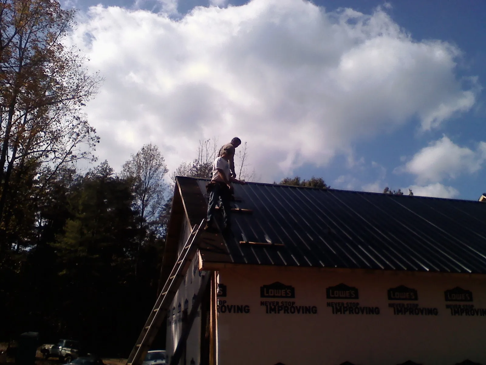 Roofer fastening dark metal panels high against a cloudy sky, from a Roof Inspection job in Campbell