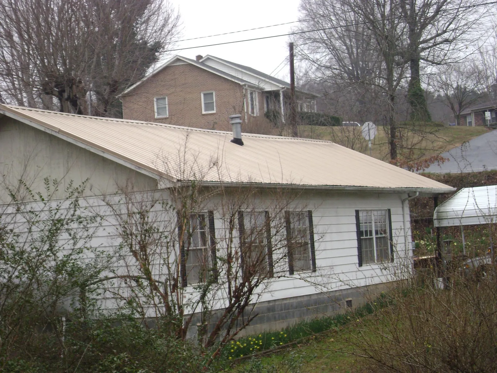 Tan metal roof on a white sided house set into a hillside — Commercial Roofing by Roofing Brothers in Campbell